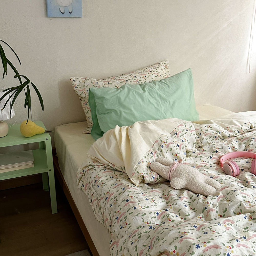 Colorful meadow floral cotton bedding with a mint green accent pillow and cream reverse, shown on a bed - Roomden