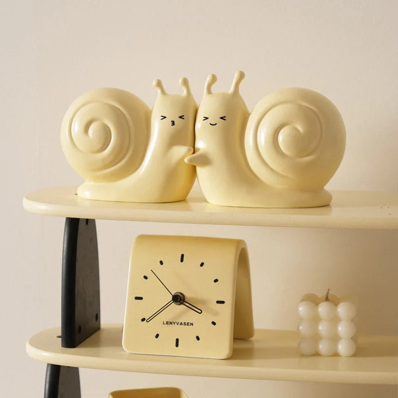 Pastel yellow snail ceramic bookends displayed on a tiered shelf with a matching clock and a bubble candle - RoomDen.