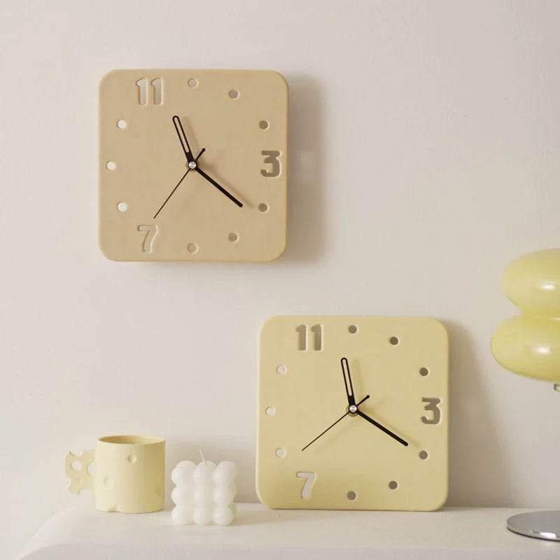 Two Butter Yellow ceramic table clocks, one on a shelf and one on a wall in a softly lit room - RoomDen.