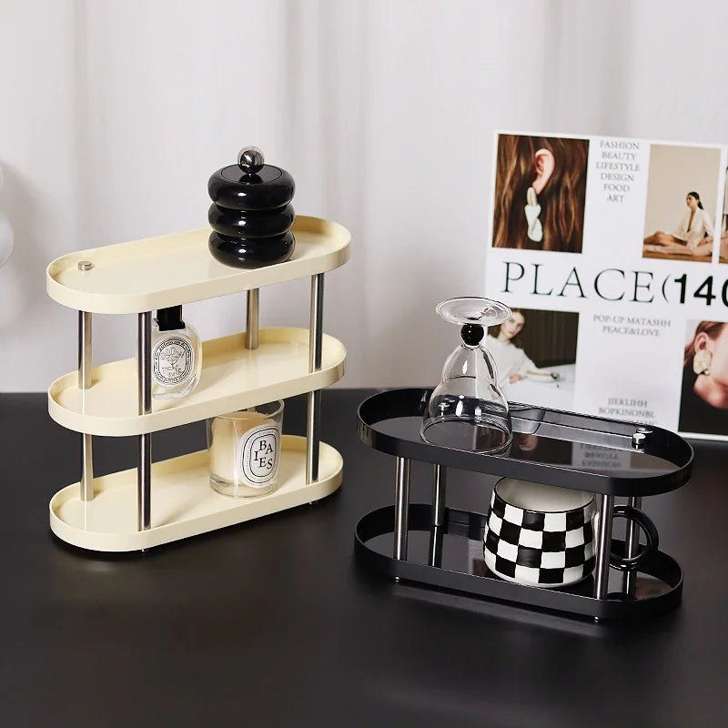 Two tiered makeup organizers, one cream and one black, shown on a desk with decor items. - RoomDen