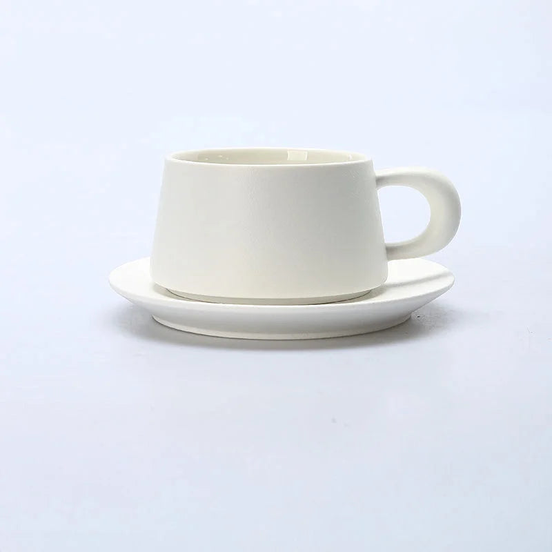 A Pure White matte ceramic coffee cup with a chunky handle and matching saucer on a white background. - RoomDen