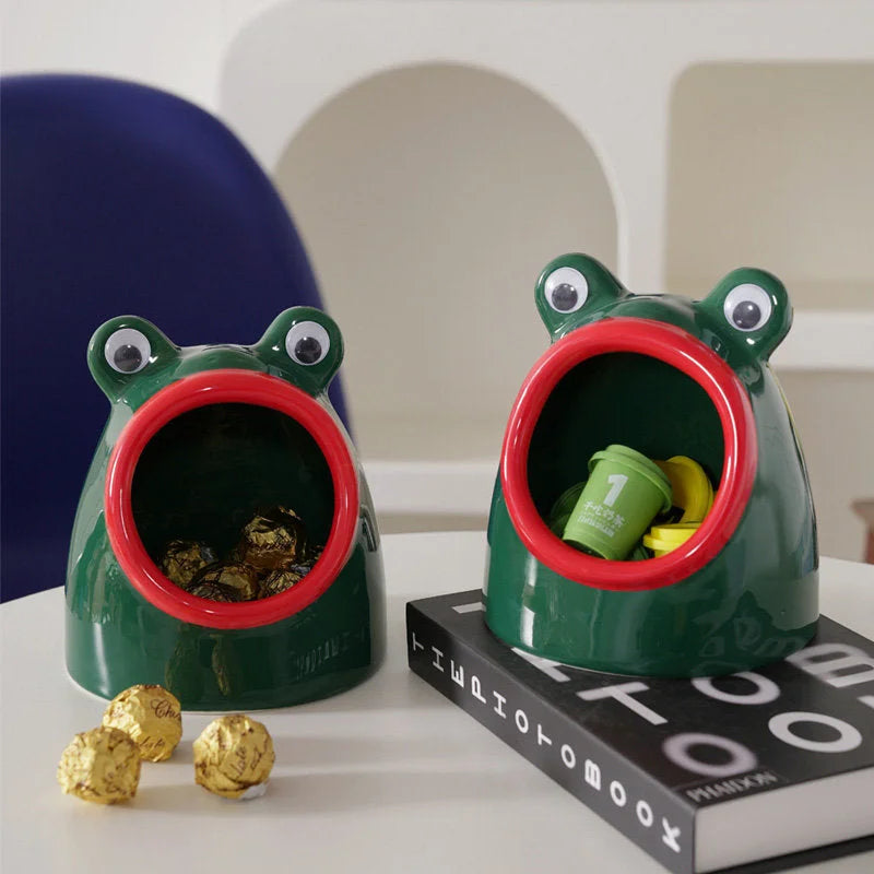 Two green frog organizers on a white table, one filled with chocolates, next to a black book. - RoomDen