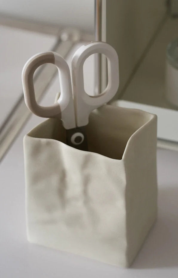 Close-up of a cream crumpled ceramic organizer holding a pair of modern white scissors. - RoomDen