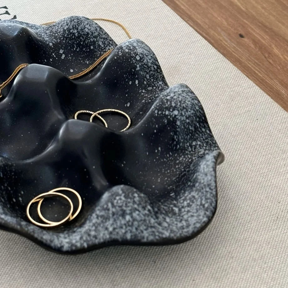 Close-up shot showing the speckled texture and gold rings in the Black Wavy Ceramic Jewelry Dish. - RoomDen