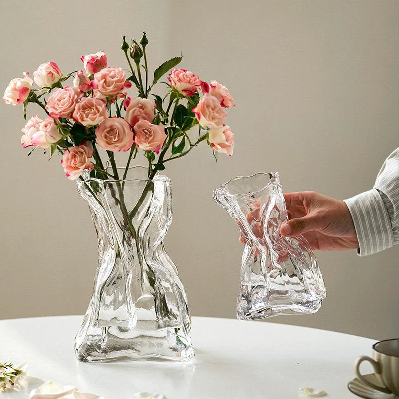 Lifestyle scene of the large and small clear Sculptural Crumpled Glass Vases, one holding pink roses. - RoomDen