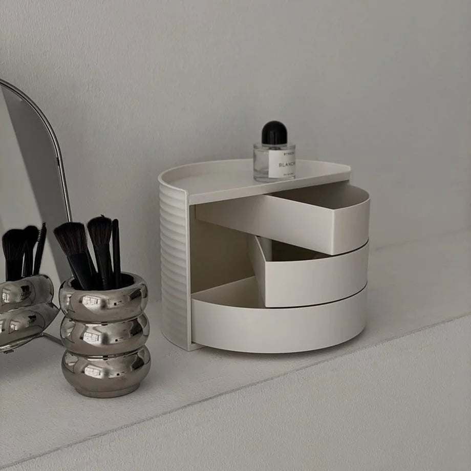 Cream white rotating makeup organizer with swivel drawers open, next to a silver brush holder. - RoomDen
