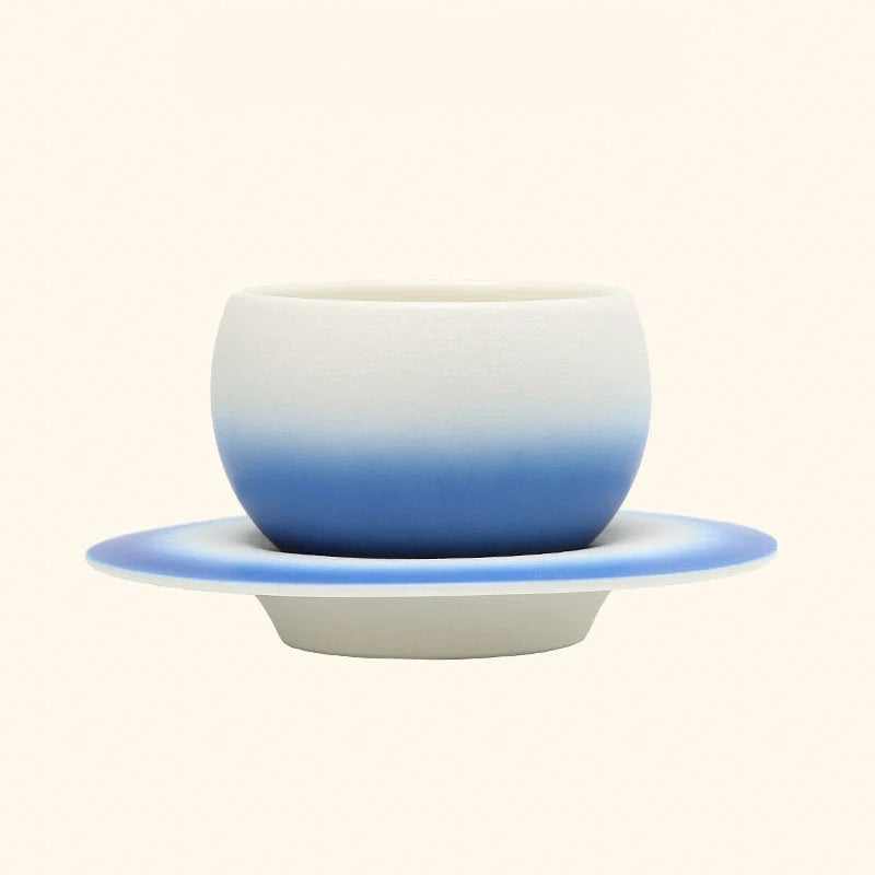 The Sky Blue Ombre Ceramic Cup displayed on its matching Saturn-ring saucer. - RoomDen