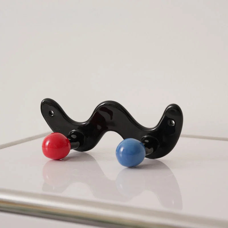 Glossy black wavy wall hook with one red and one blue ball on a white surface.