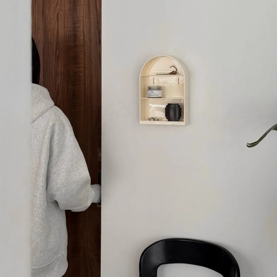 Cream arched wall shelf mounted in a minimalist entryway next to a wooden door - RoomDen.