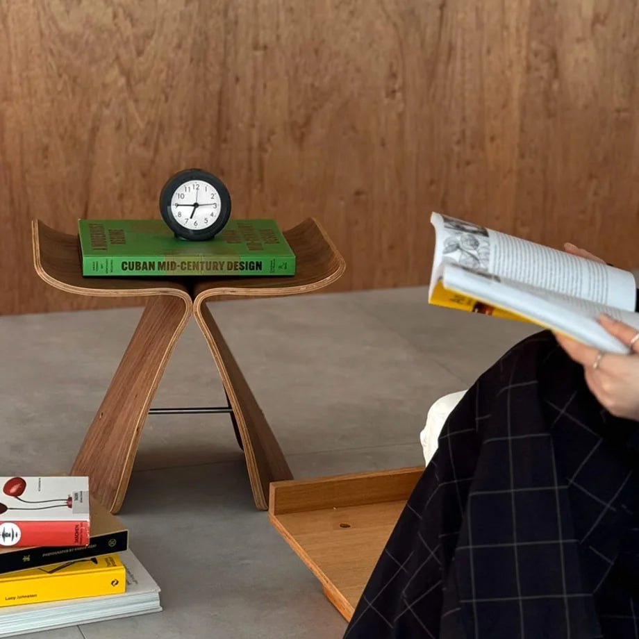 Lifestyle scene showing the black analog alarm clock on a butterfly stool next to a person reading. - RoomDen