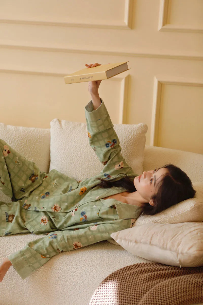 Playful shot of woman holding book up while lying down in green animal print sleepwear
