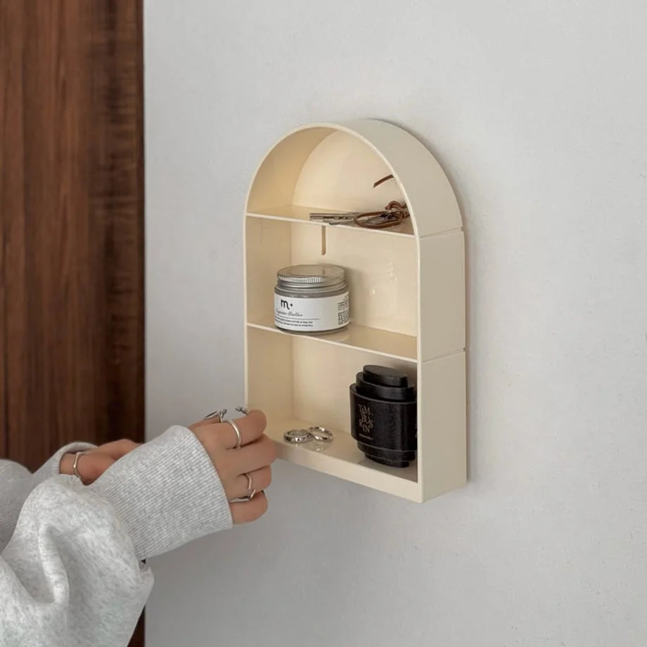 Close-up of the cream arched wall shelf holding keys and small items, with a hand reaching for it - RoomDen.