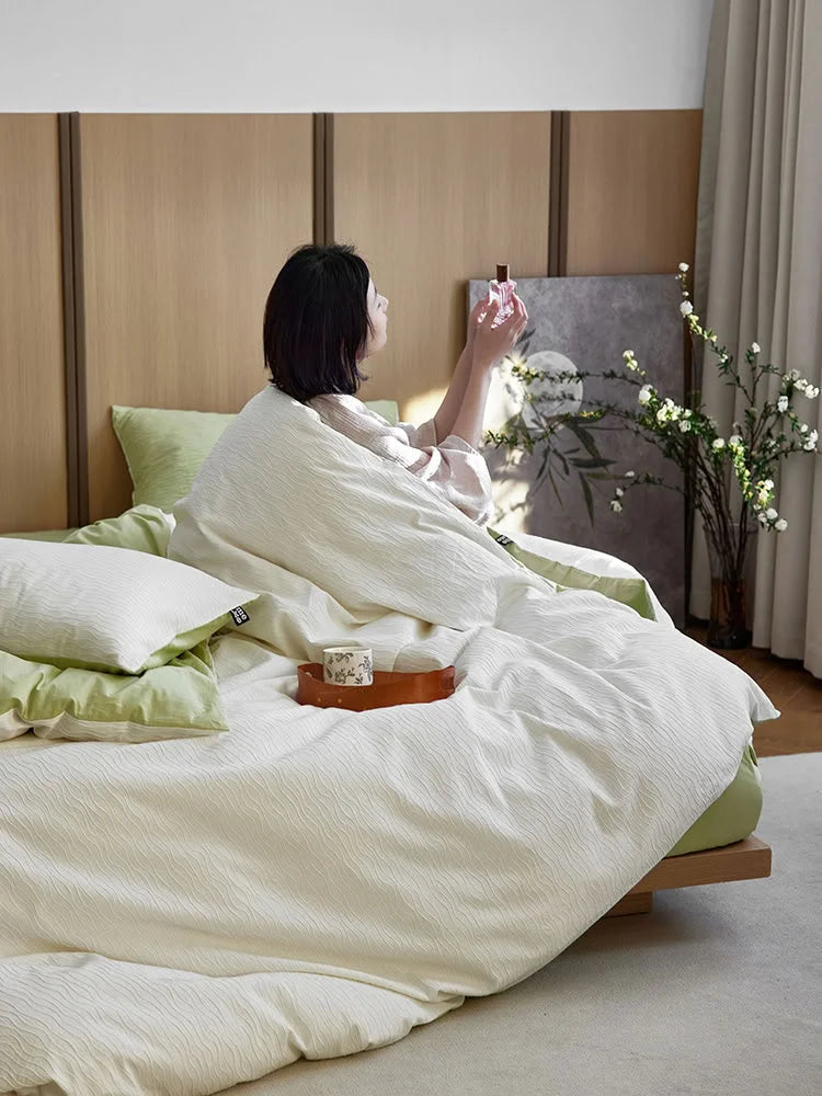 Lifestyle scene with a person sitting up in the Cream White & Matcha Green bedding. - RoomDen
