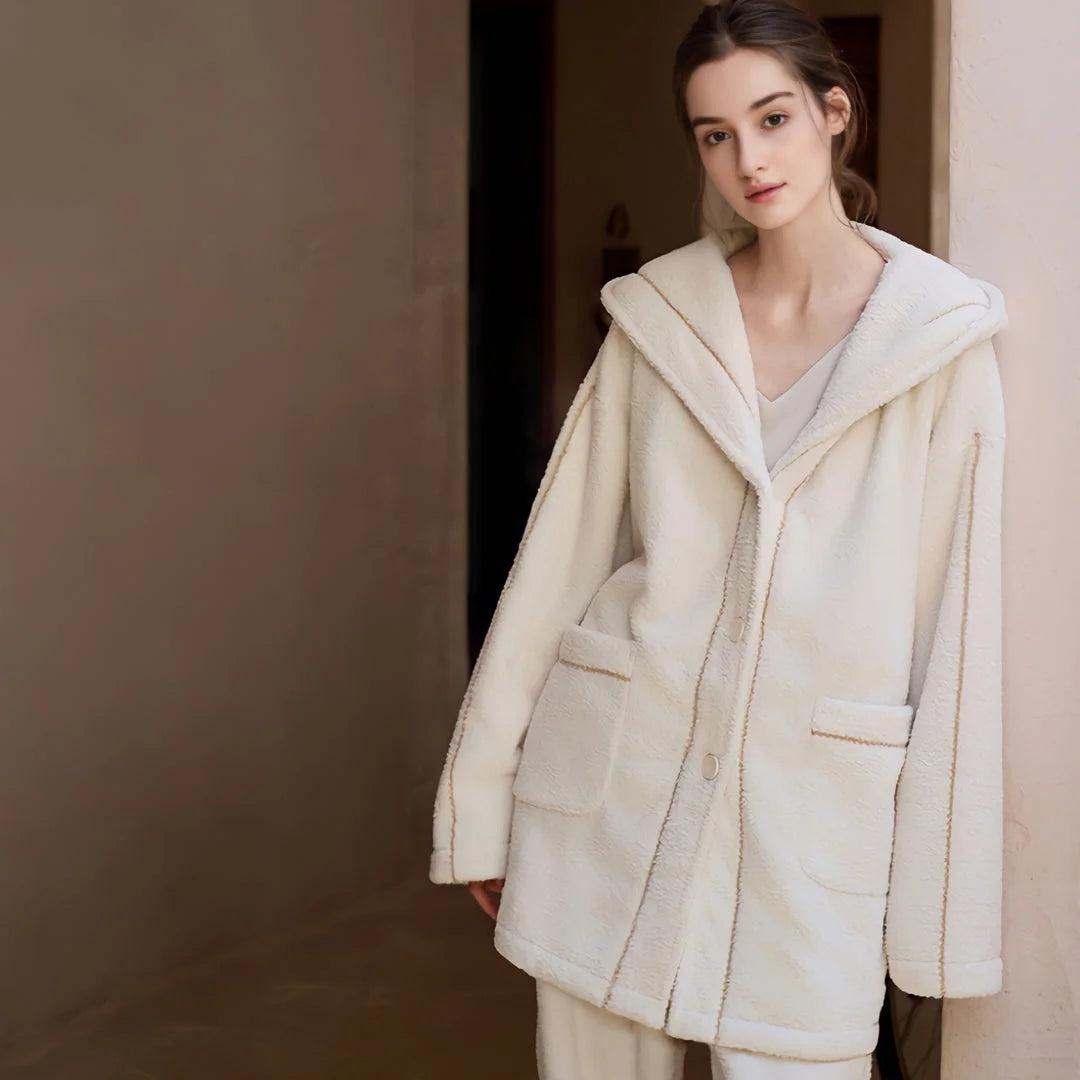A closer view of a model in a hallway wearing a soft, creamy white hooded pajama set - RoomDen.