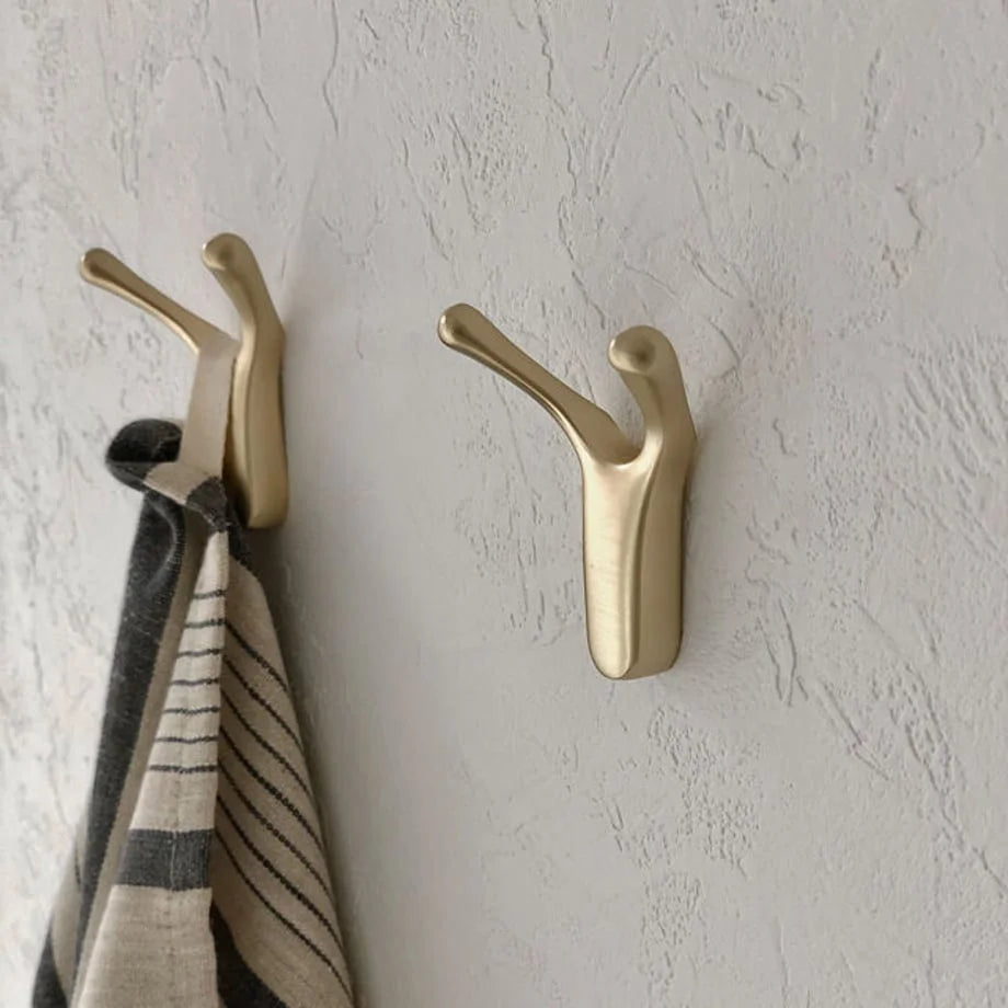 Close-up detail of two gold branch-shaped metal wall hooks, showing their smooth, curved design - RoomDen