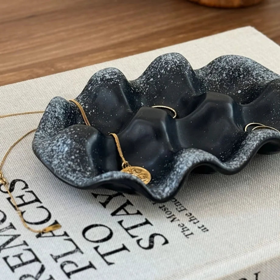 Detailed view of the black speckled ceramic and wavy design holding a gold necklace and ring.