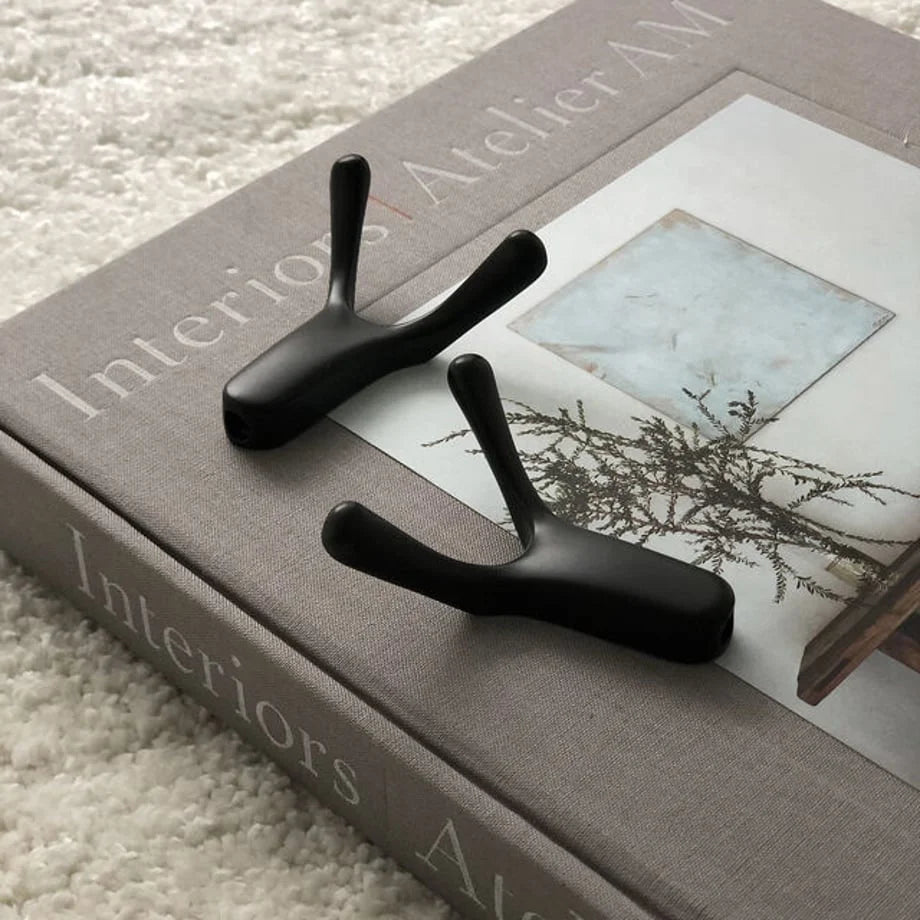 Variant Product shot: Two matte black branch-shaped hooks resting on a grey 'Interiors Atelier AM' book - RoomDen