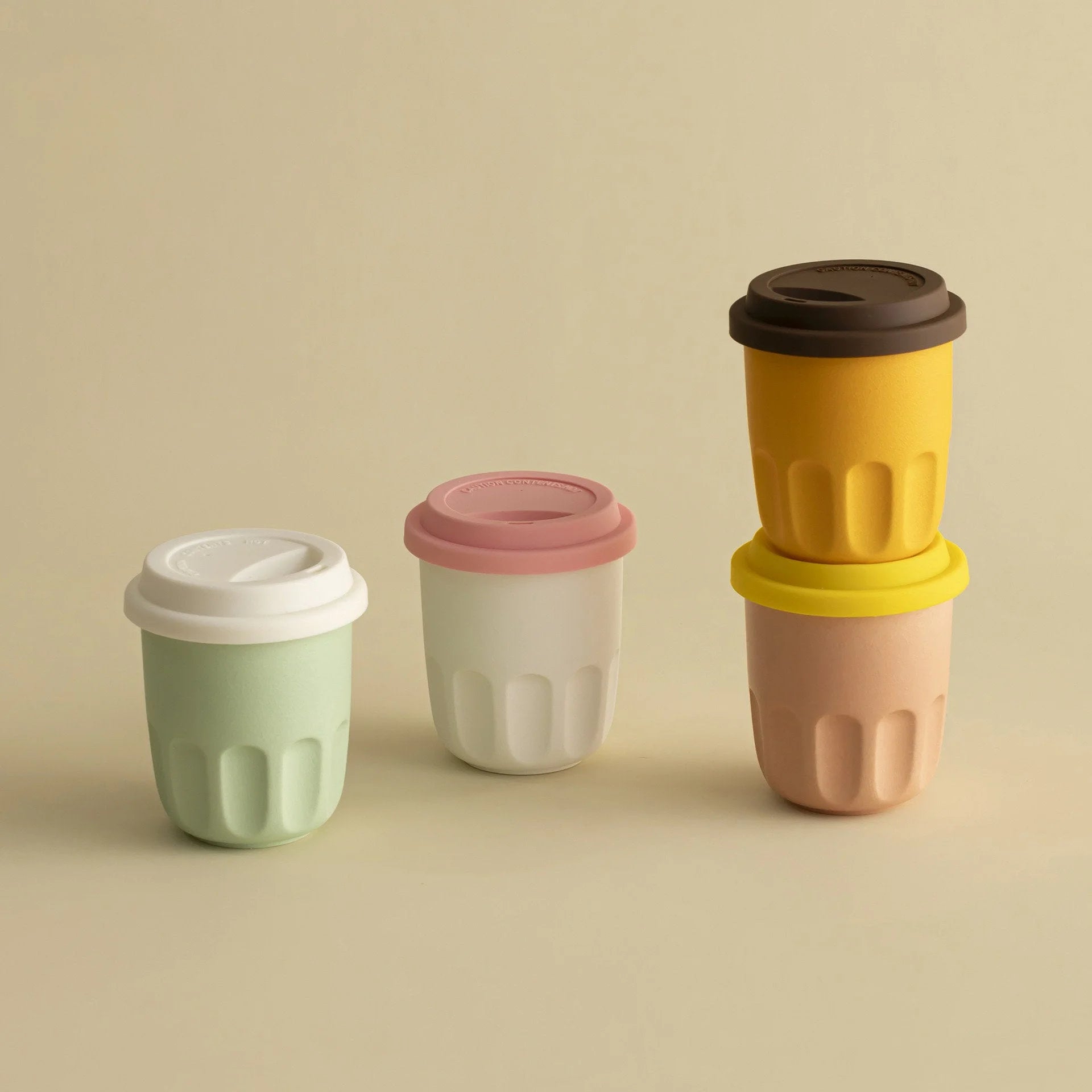 Four frosted ceramic reusable coffee cups in mint green, cream white, mustard yellow, and peach beige on a neutral background. - RoomDen
