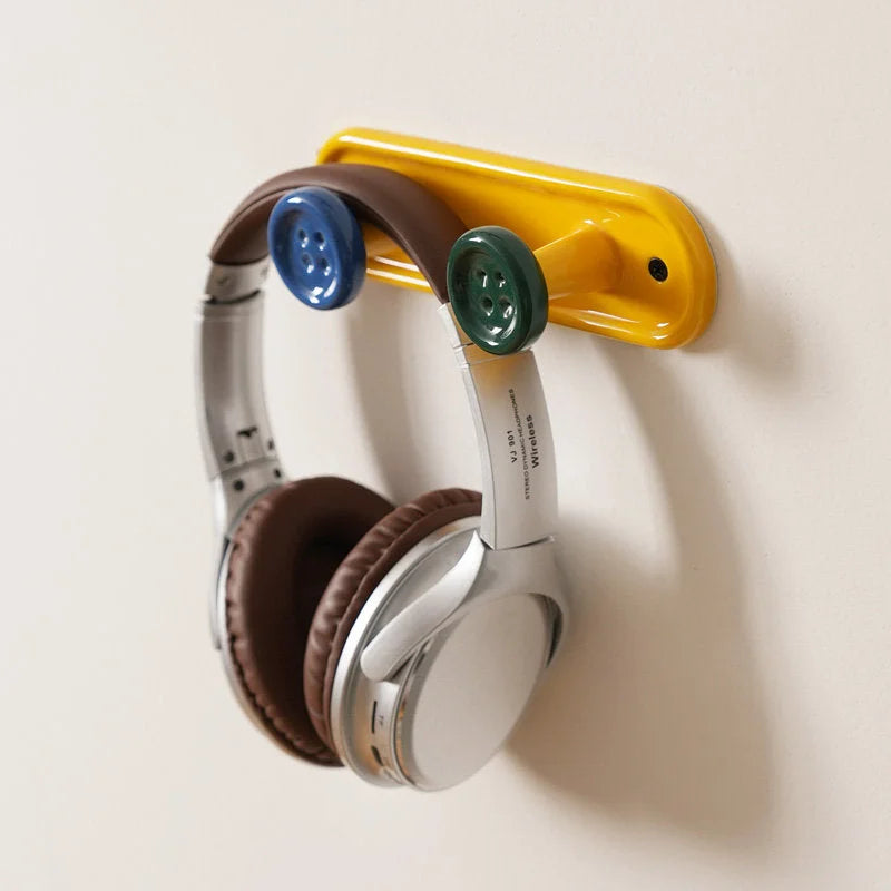 Detail shot of the yellow 2-hook button wall rack holding a pair of silver headphones. - RoomDen