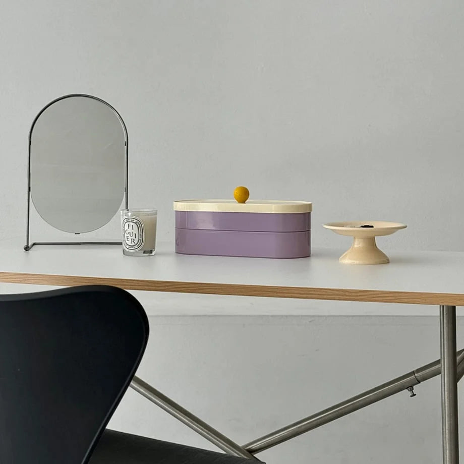 Wide view of the lavender and cream two-tier makeup organizer on a light wood desk with a black chair and mirror.