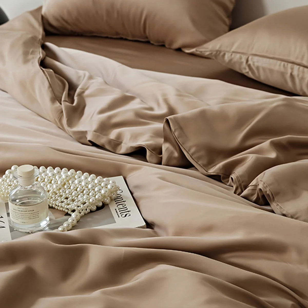 A lifestyle detail of the Mocha Brown bedding with a book and a string of pearls.