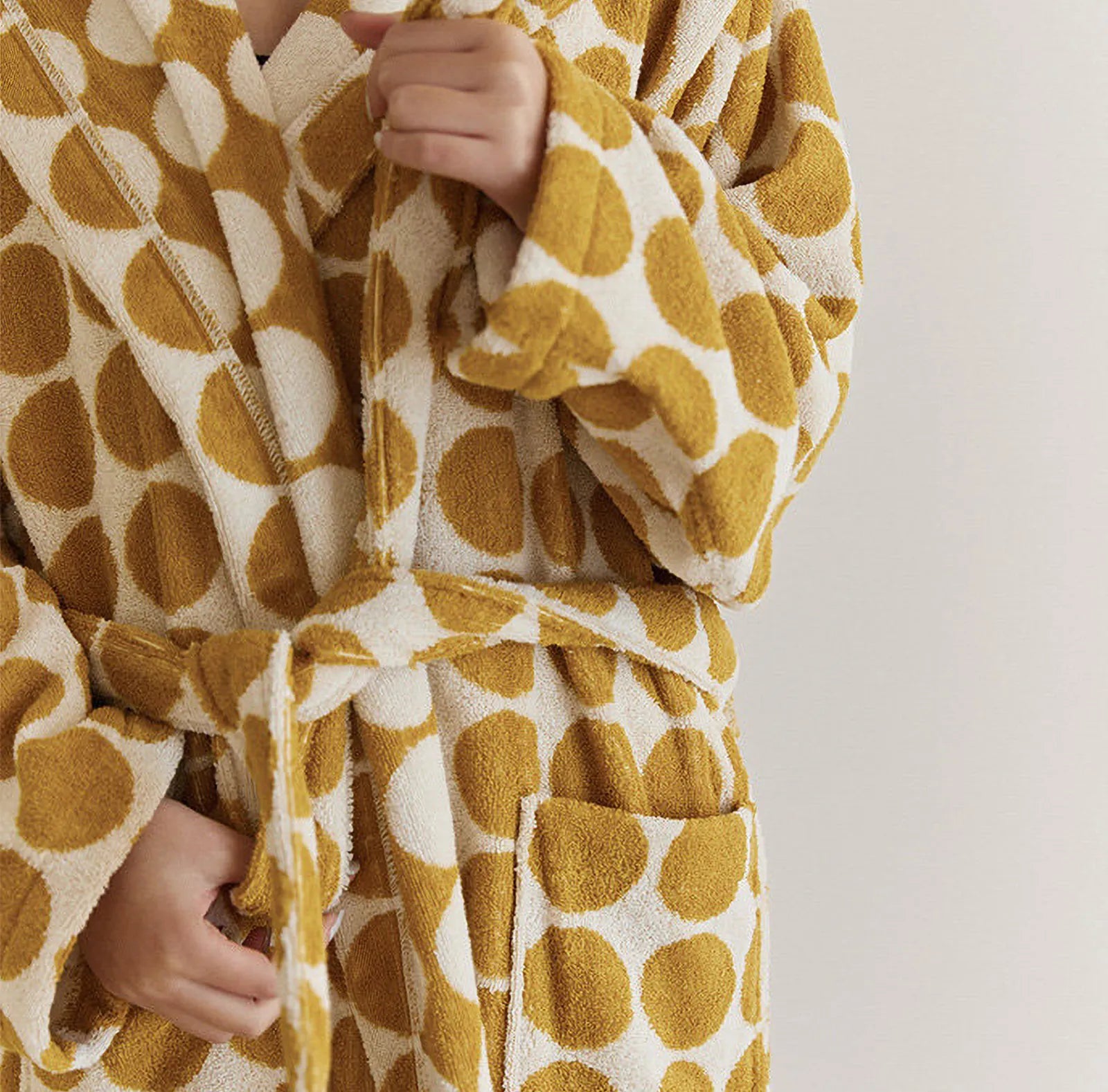 Close-up of person tying the sash belt of a plush yellow polka dot terry cloth robe - RoomDen