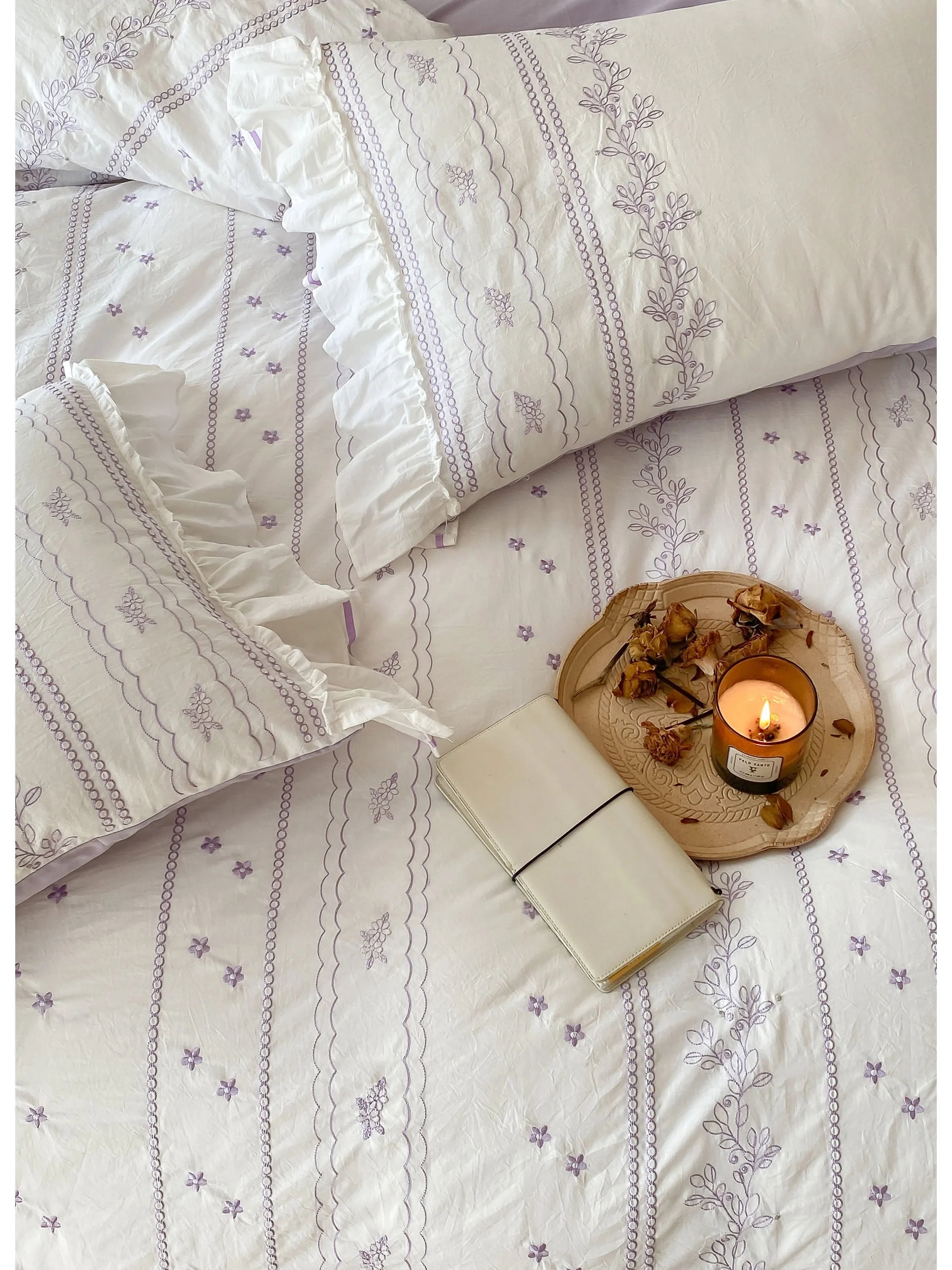 Top-down view of the Lavender embroidered duvet cover with a journal and candle.