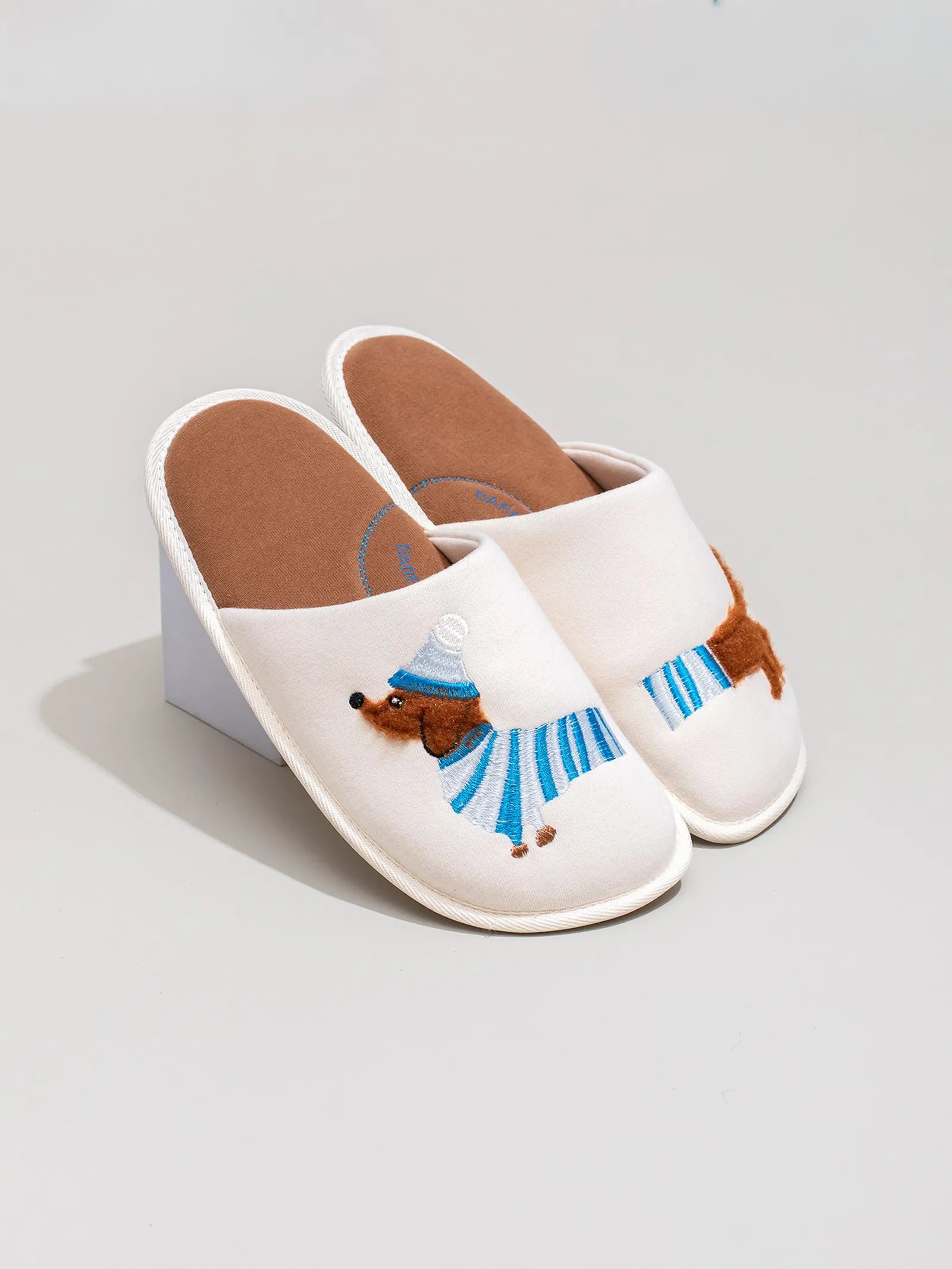 White embroidered dachshund slippers displayed on a prop showing side profile and brown insole