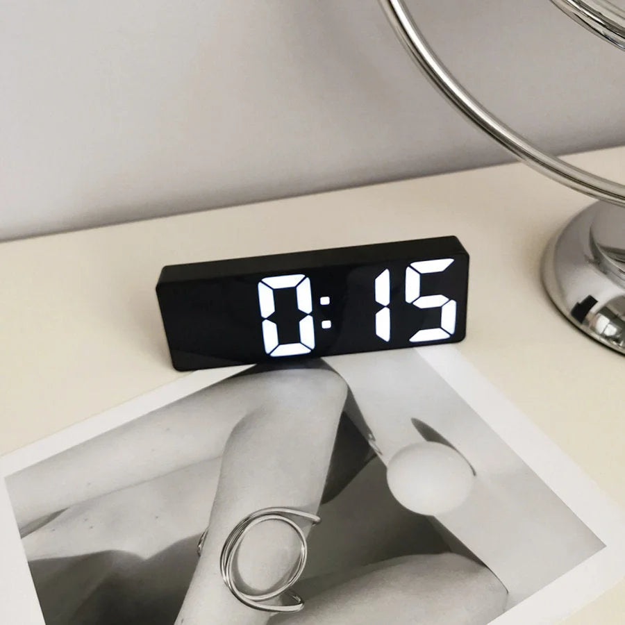 Close-up of the black Sleek Mirrored Acrylic LED Table Clock on a white desk with modern art. - RoomDen