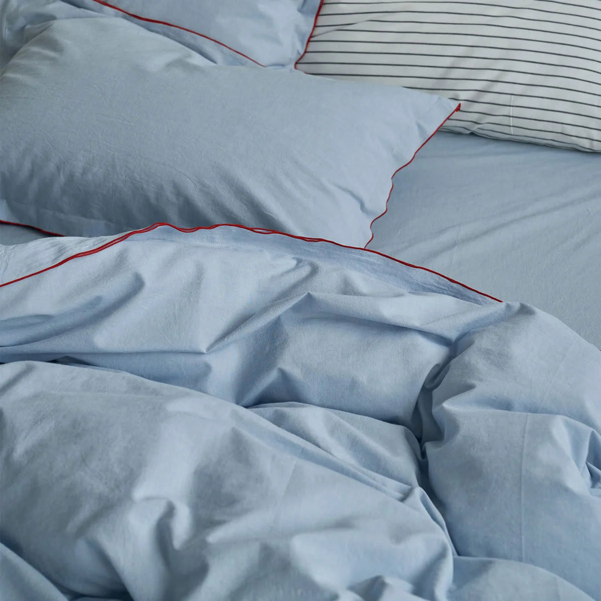 Close-up of the soft texture and red contrast piping on a sky blue washed cotton duvet cover.