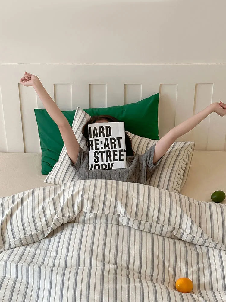 A person relaxing in bed under the cozy Grey Pinstripe Washed Cotton Duvet Cover. - RoomDen