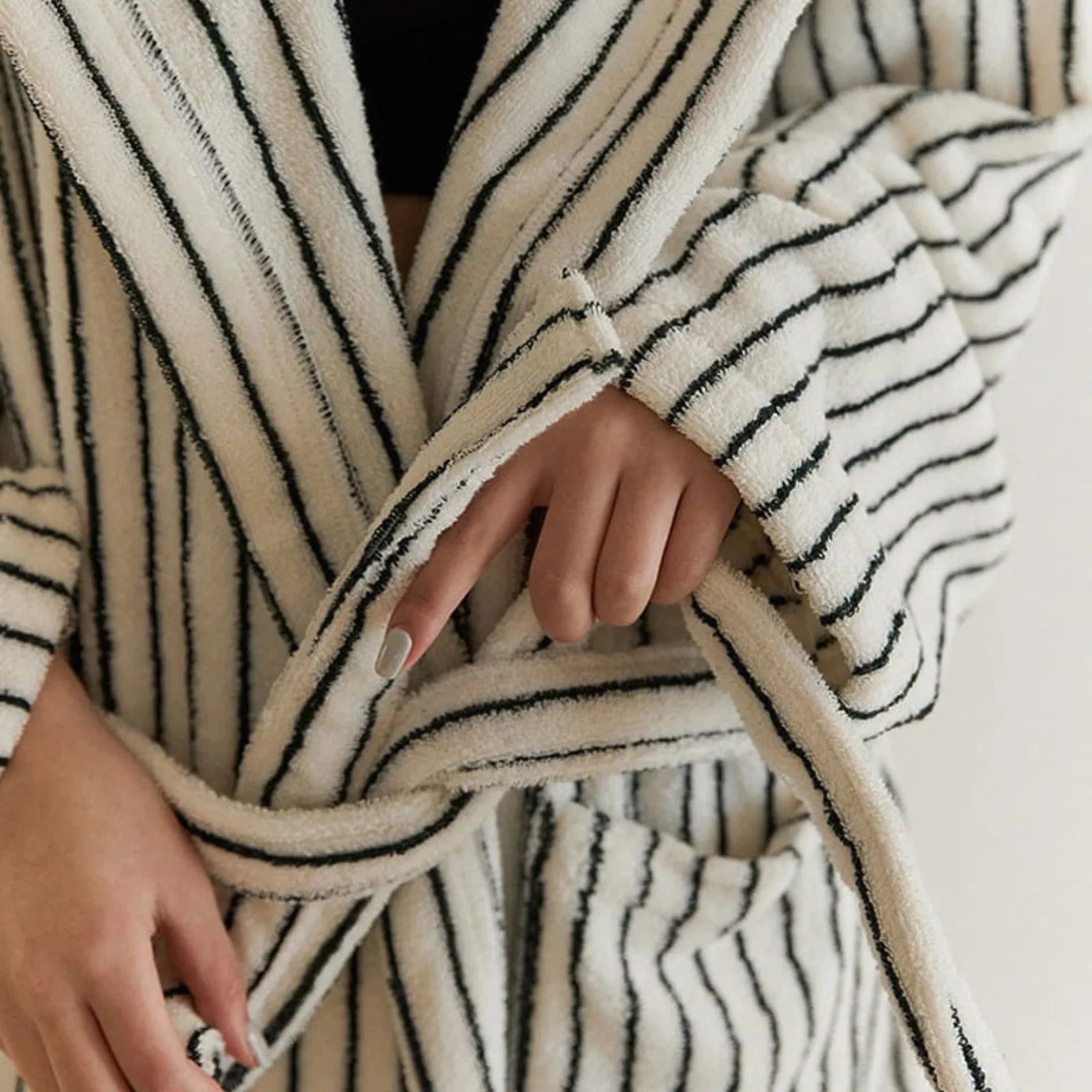 Close-up detail of the long-staple cotton terry fabric texture and hand tying the waist sash of the striped robe.