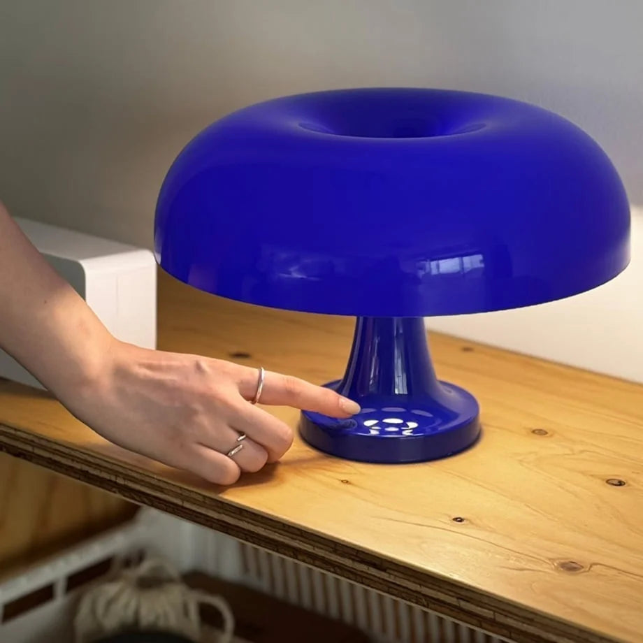Close-up of a hand touching the base of a cobalt blue mushroom lamp to turn it on - RoomDen.