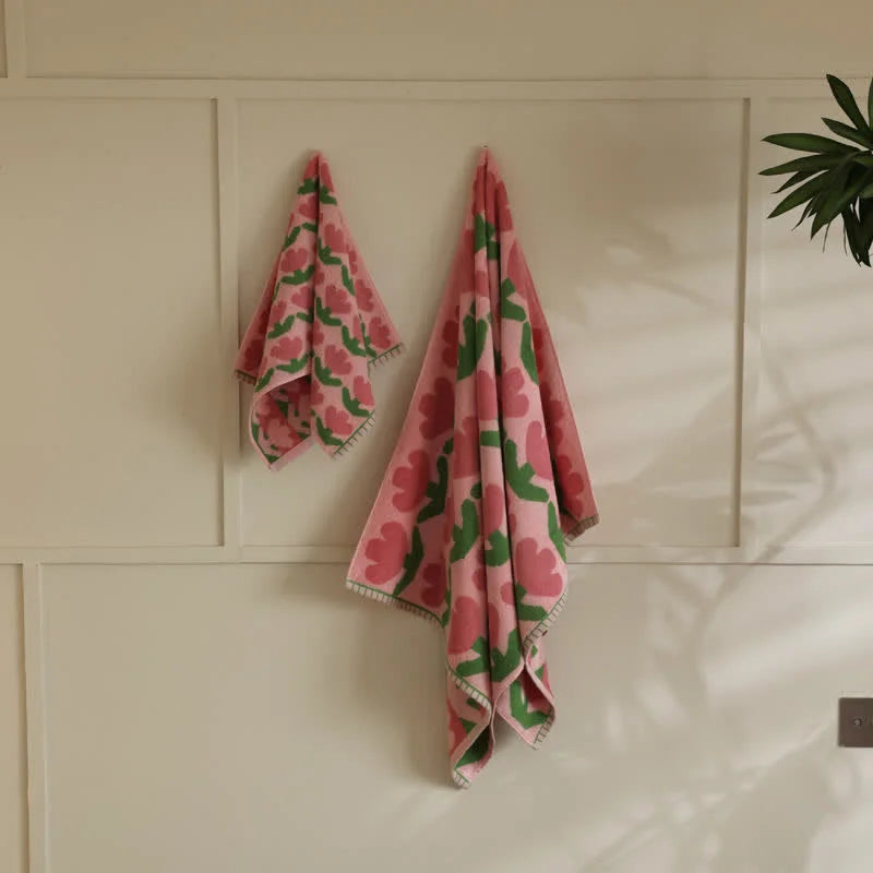 Plush Tulip Floral Cotton Towel Set in pink and green hanging on a white paneled wall - RoomDen