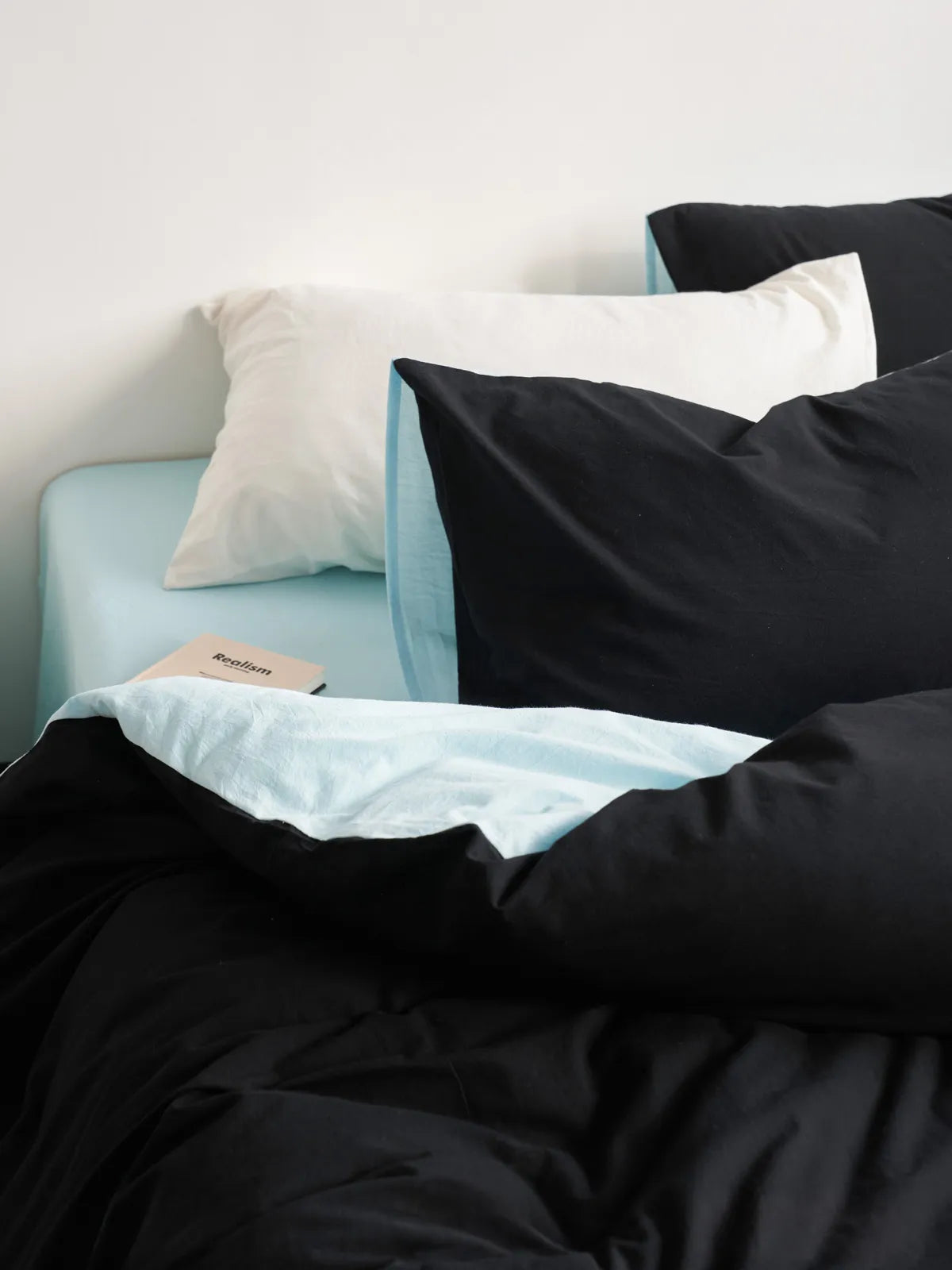 Close-up of the Reversible Two-Tone Washed Cotton Bedding Set showing the black duvet cover folded over to reveal the cyan interior. - RoomDen