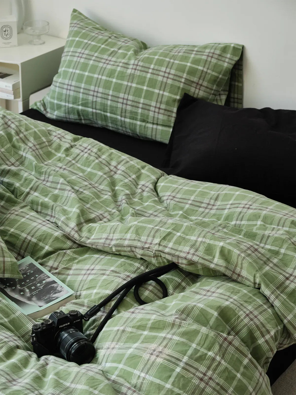 A close-up of the Soft Matcha Green Plaid Cotton Bedding Set, with a vintage camera and book resting on the rumpled duvet cover. - RoomDen