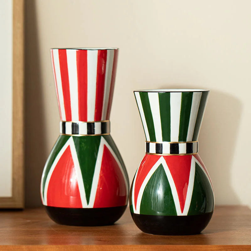 Two variations of the harlequin striped ceramic vase, one with red stripes and one with green stripes, shown side-by-side on a wooden dresser. - RoomDen