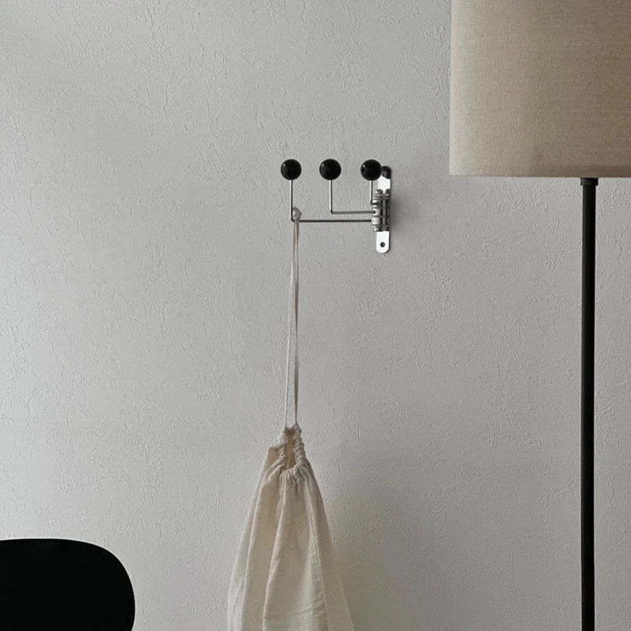 Angled view of the black triple-arm swivel wall hook against a bright, textured wall - RoomDen.