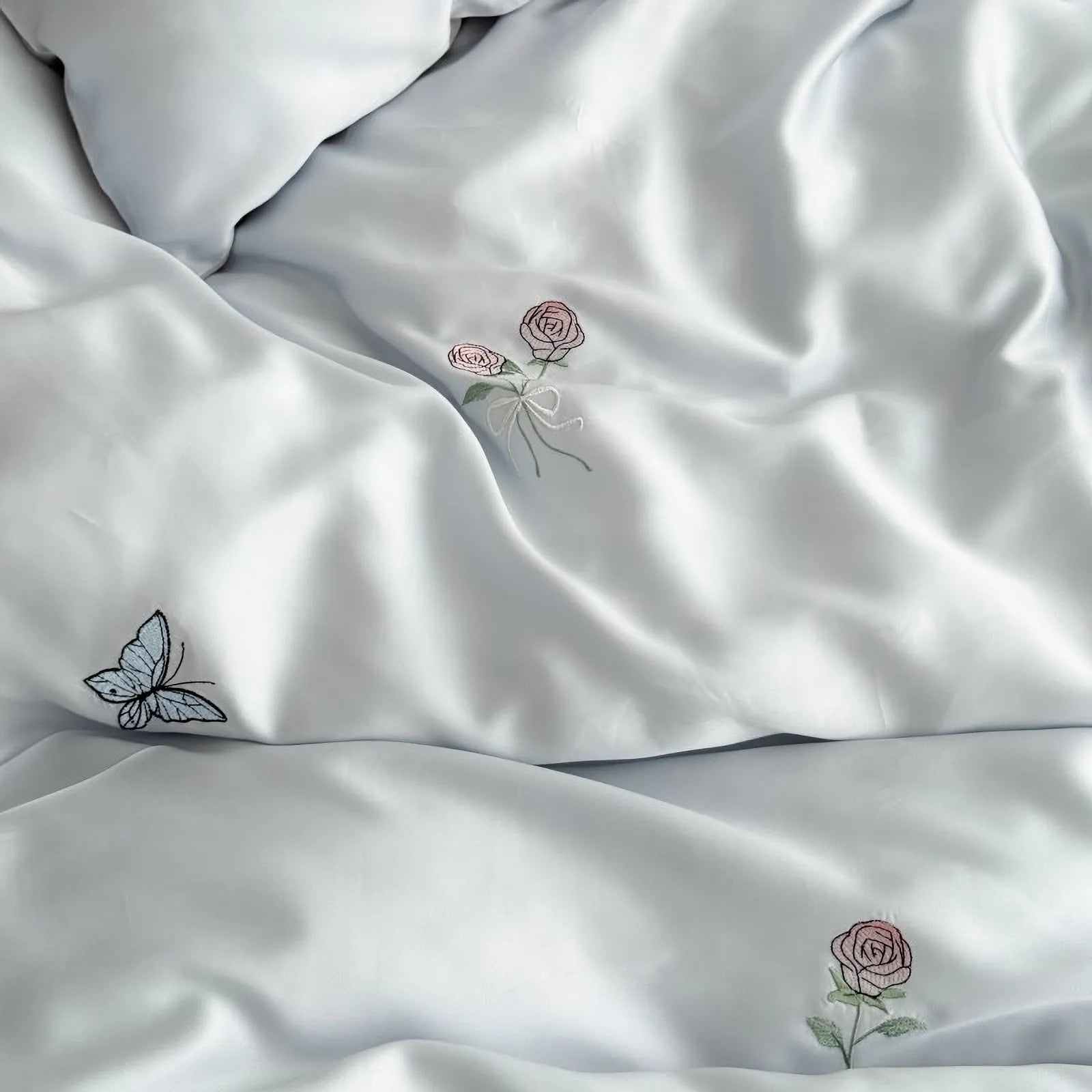 Close-up on the silky Cloud Blue Tencel duvet cover, highlighting the delicate pink rose and blue butterfly embroidery. - RoomDen