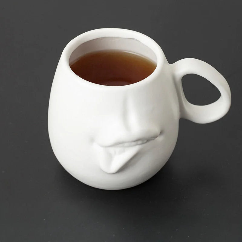 Close-up of the matte white abstract face mug filled with tea against a dark background.