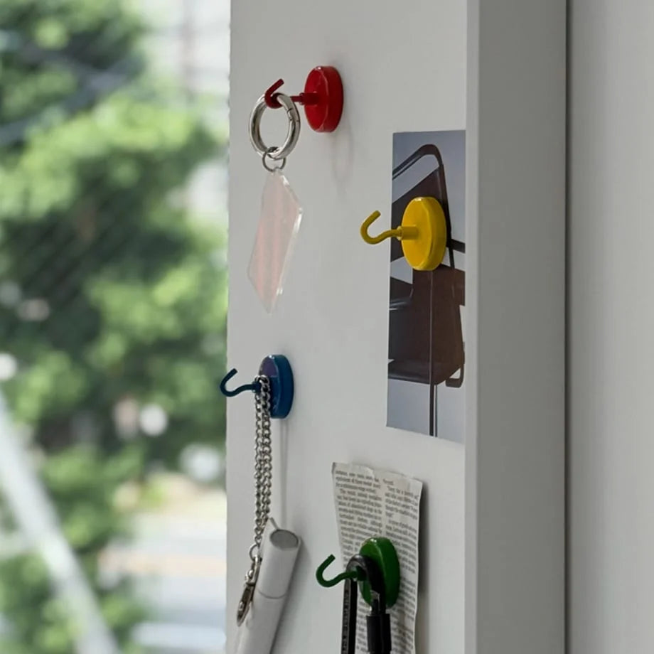 Colorful magnetic metal hooks in red, yellow, blue, and green on a white metal surface holding keys and notes - RoomDen