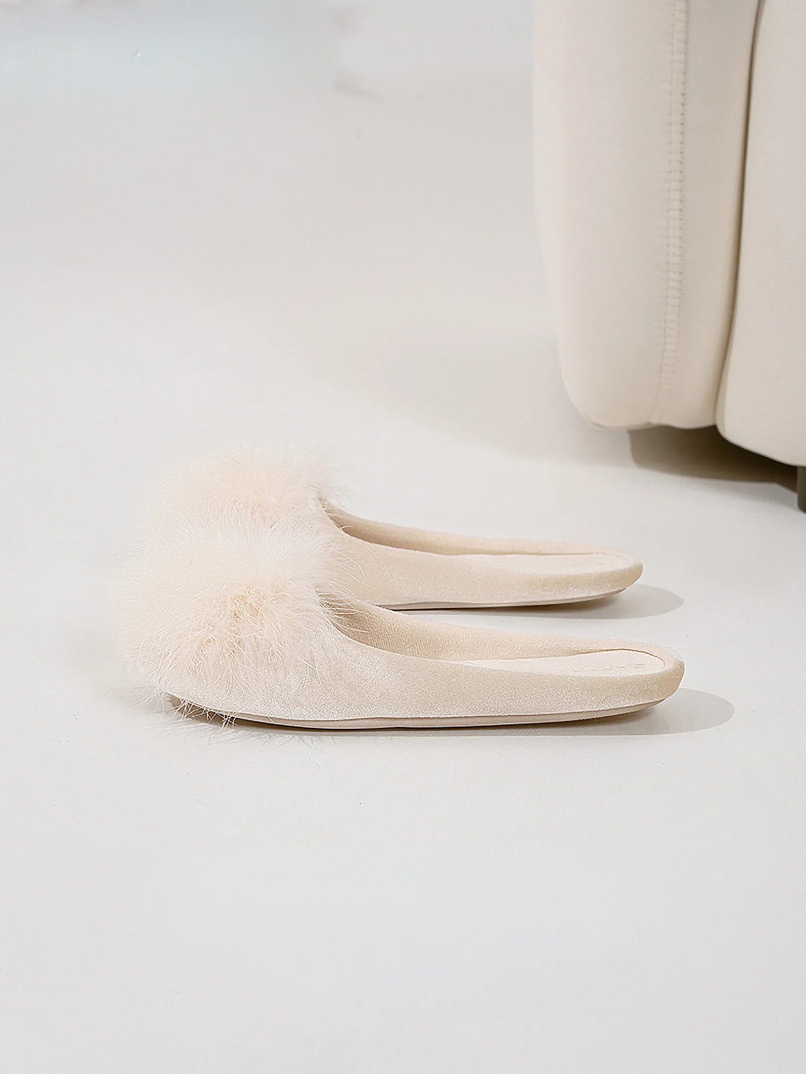 Pair of beige fluffy house slippers placed on white floor - RoomDen