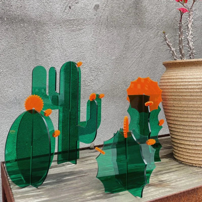 Two green acrylic cactus decorative objects displayed on a wooden surface with a terracotta pot in the background - RoomDen