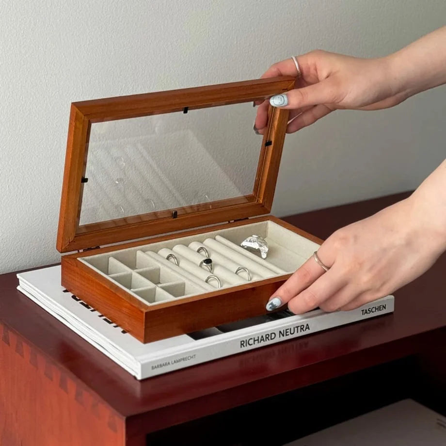 A person opening a polished wood jewelry organizer with a glass lid, revealing rings inside. - RoomDen