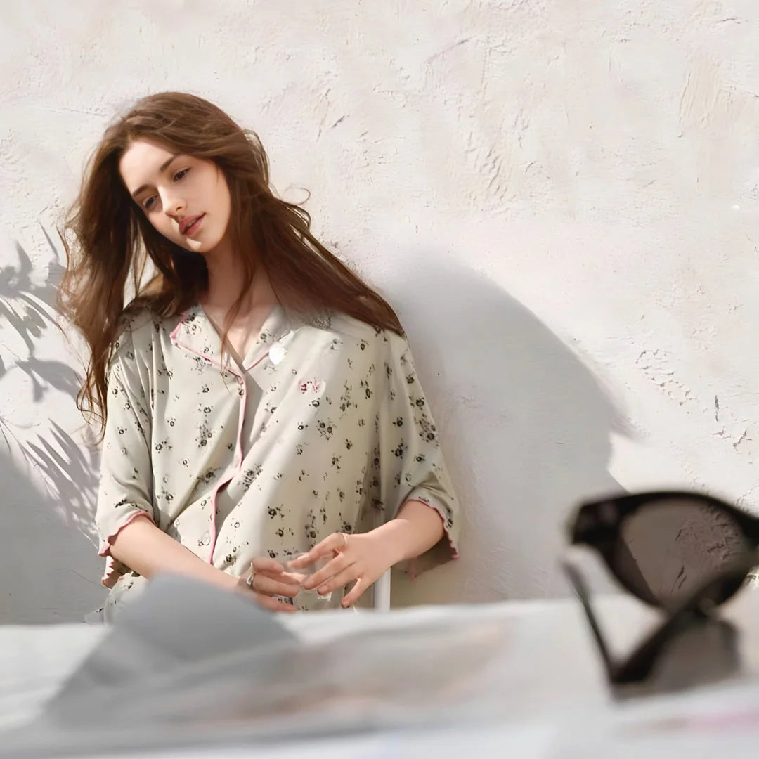 Lifestyle shot of the model sitting at a table, wearing the sage green modal pajama set in soft lighting. - RoomDen