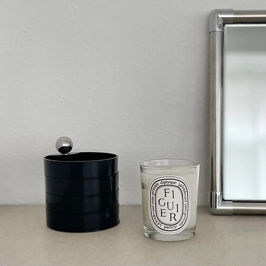 The Matte Black 4-tier jewelry organizer closed and placed next to a silver-framed mirror. - RoomDen