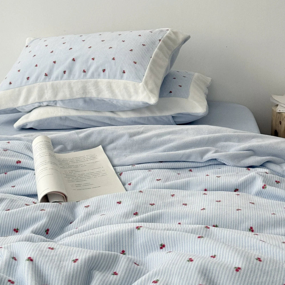 Close-up of a plush light blue cherry pinstripe flannel fleece bedding set with an open book resting on the duvet cover - RoomDen.