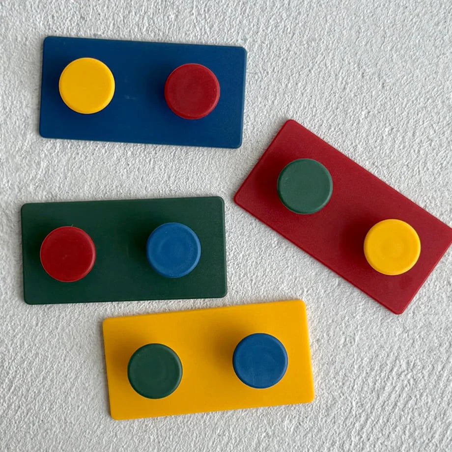Four Matte Colorblock ABS Decorative Hooks in blue, green, red, and yellow laid on a textured white surface - RoomDen.