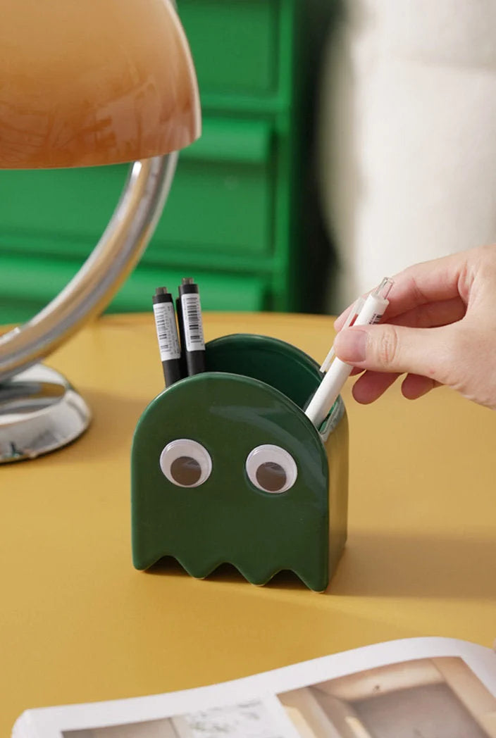 A hand placing a pen into the green Retro Ghost Ceramic Pen Holder on a desk - RoomDen.