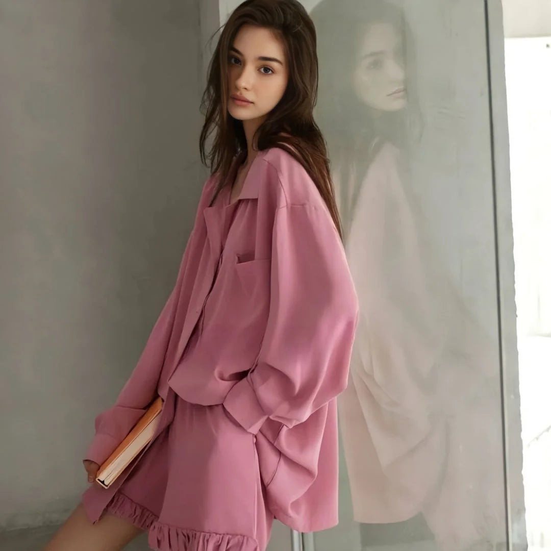 A model in the Dusty Rose pajama set standing next to a reflective surface, highlighting the garment's drape. - RoomDen